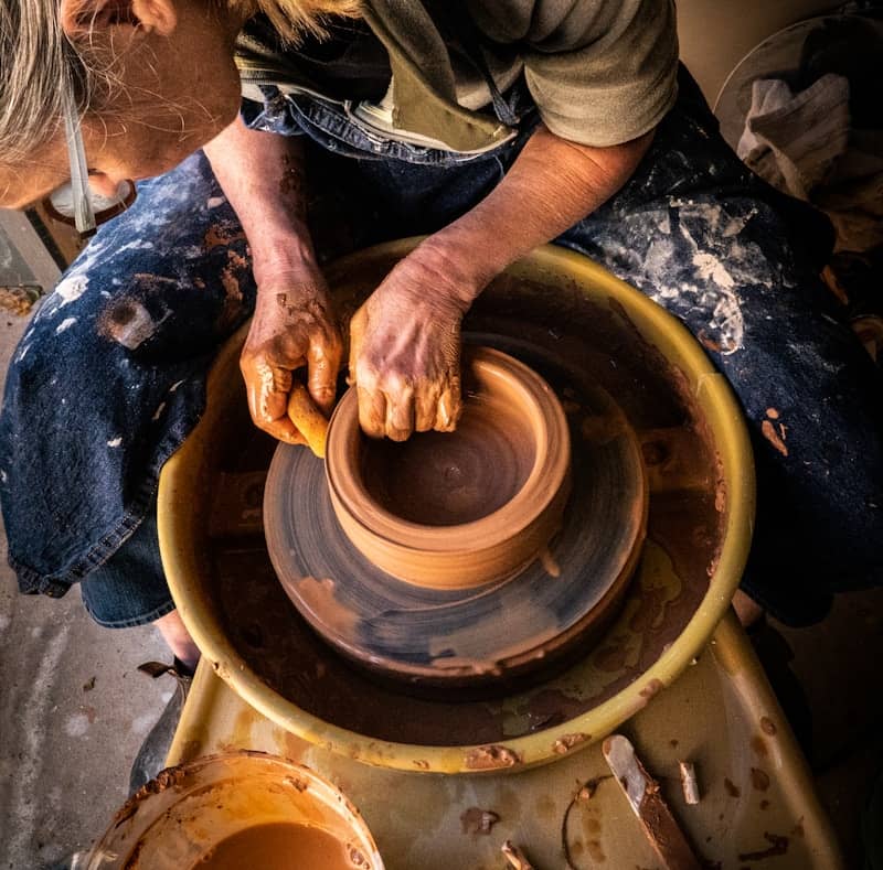 person in blue denim jeans making clay pot