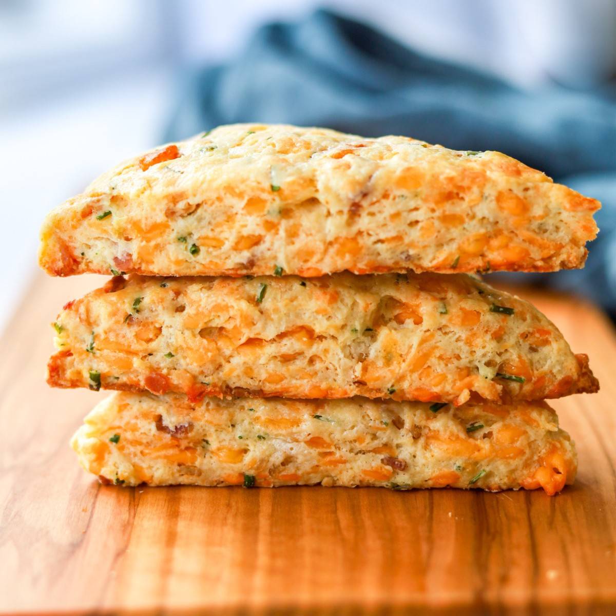 A stack of three bacon cheddar chive scones on a wood board.