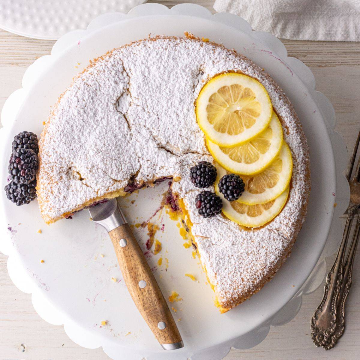 Blackberry almond cake on a cake stand with a knife.