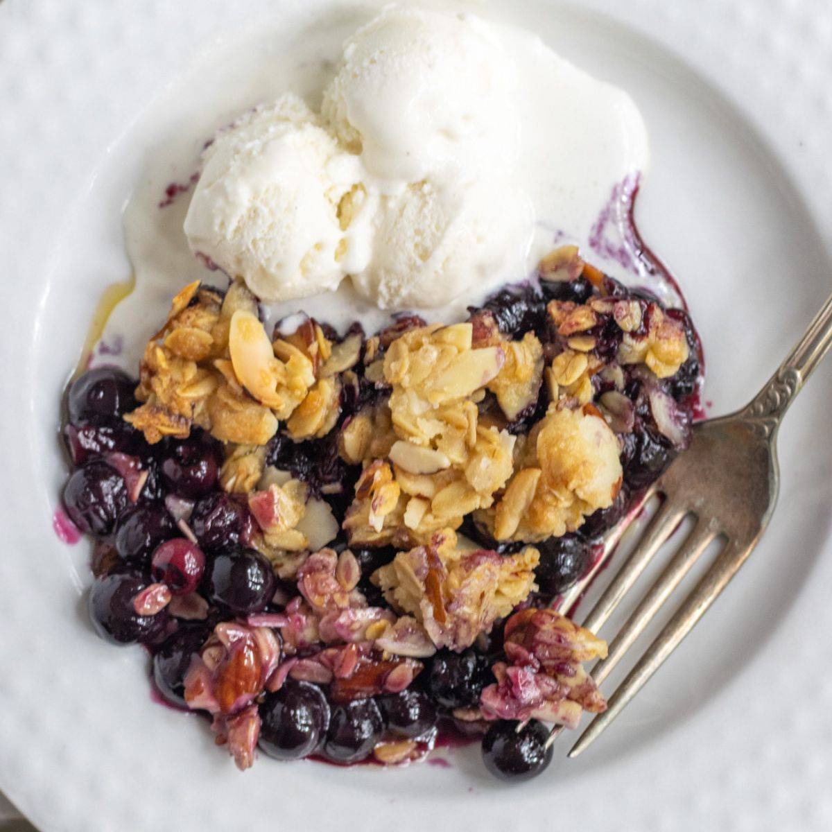 Blueberry crisp in a bowl with ice cream and a fork.