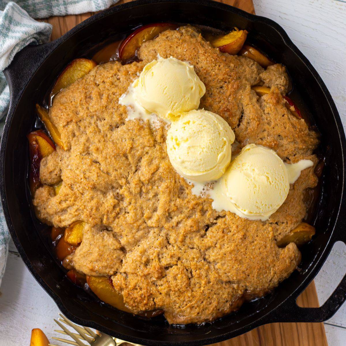 Peach cobbler in a cast iron pan with scoops of ice cream.