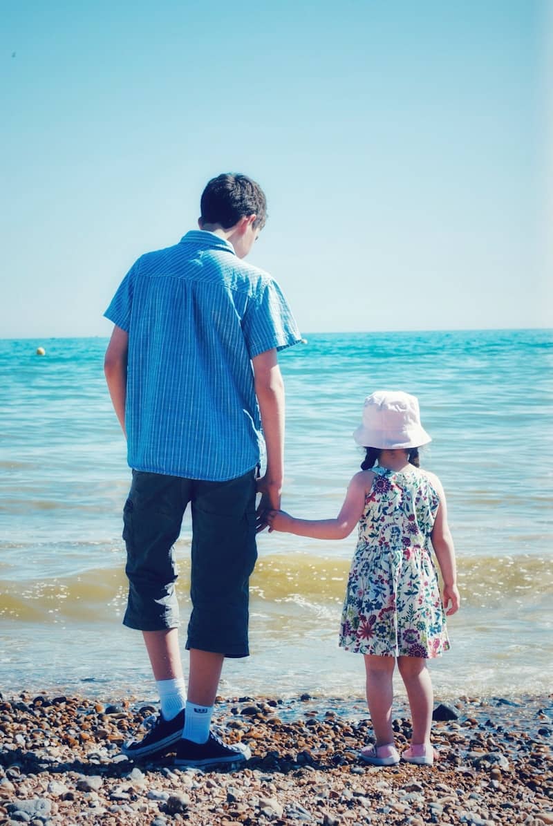 Children holding hands on a rocky beach by the sea.