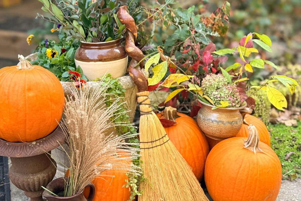 A fall corner with orange pumpkins, salt-fired pottery, cast-iron urns, a handmade broom and branches from the farm