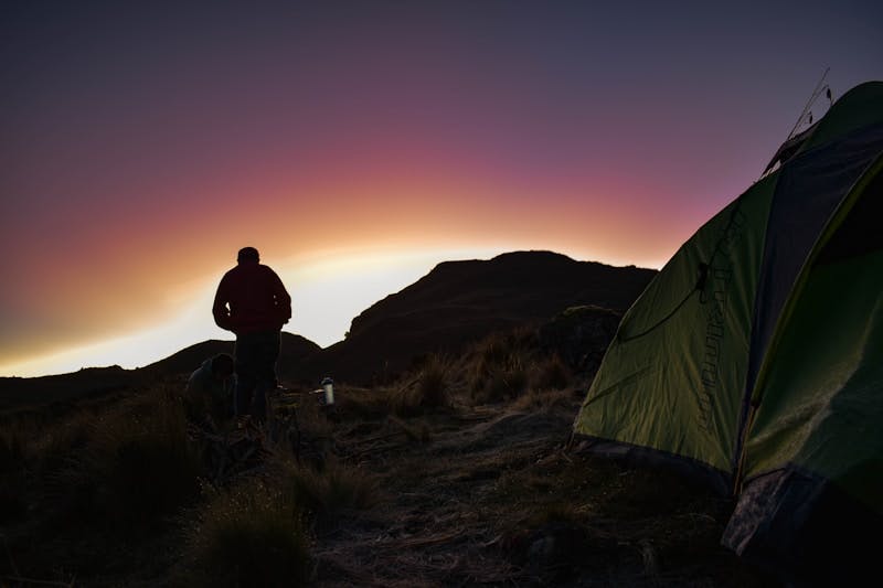 a man standing next to a tent on top of a mountain