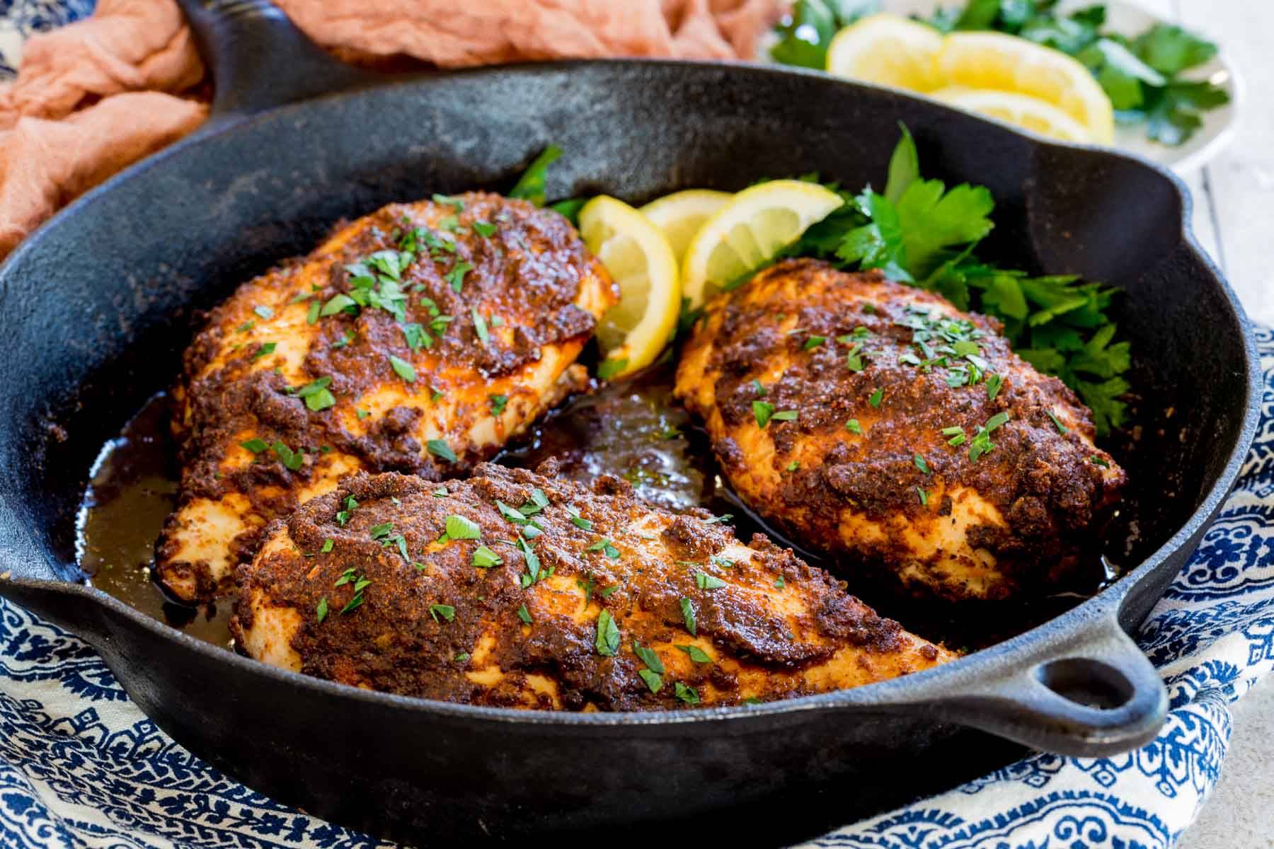 Three chicken breasts covered with a spice mixture in a cast iron skillet.