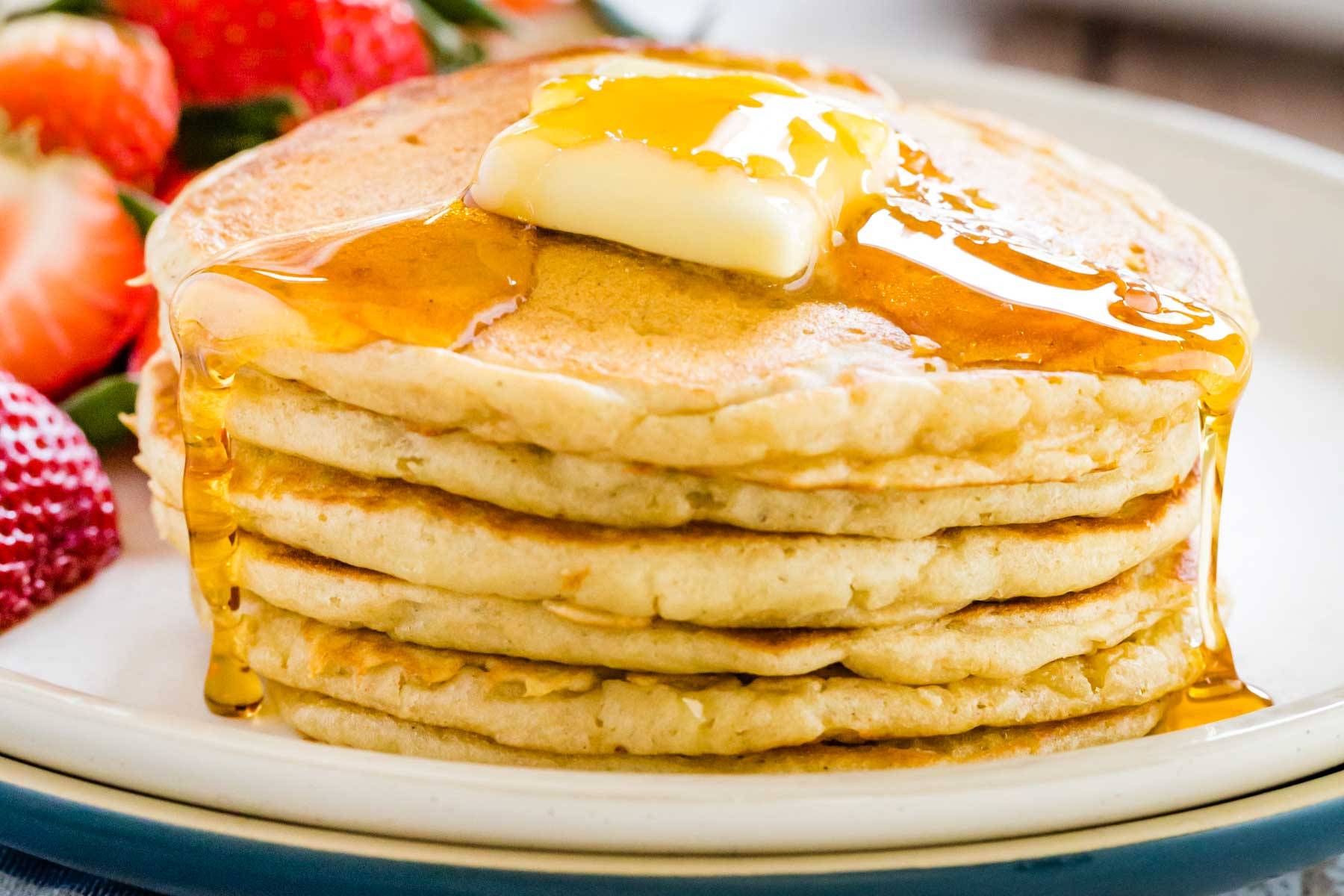 A stack of buttermilk pancakes topped with a pat of butter and syrup.