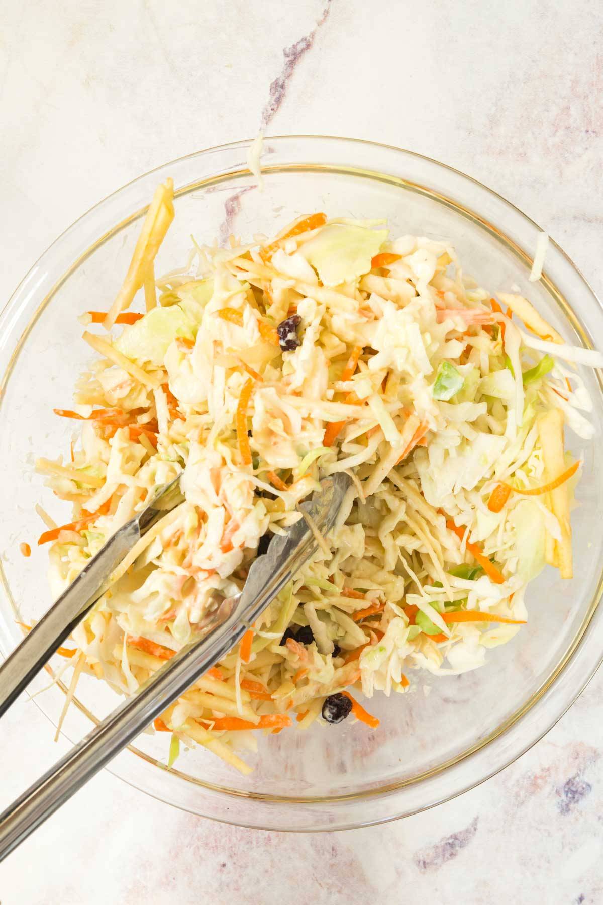 Coleslaw being tossed in a bowl.