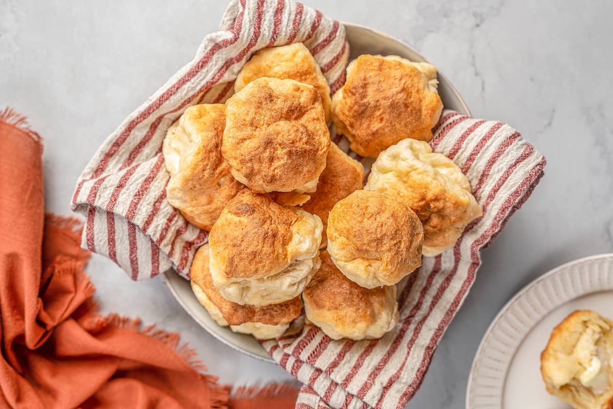 Golden brown rolls piled in a bowl lined with a striped napkin.