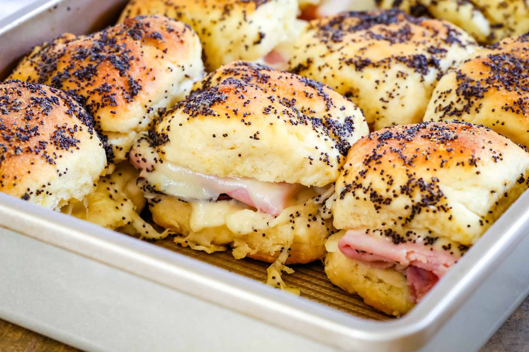 Ham and cheese slider sandwiches lined up in a baking pan.