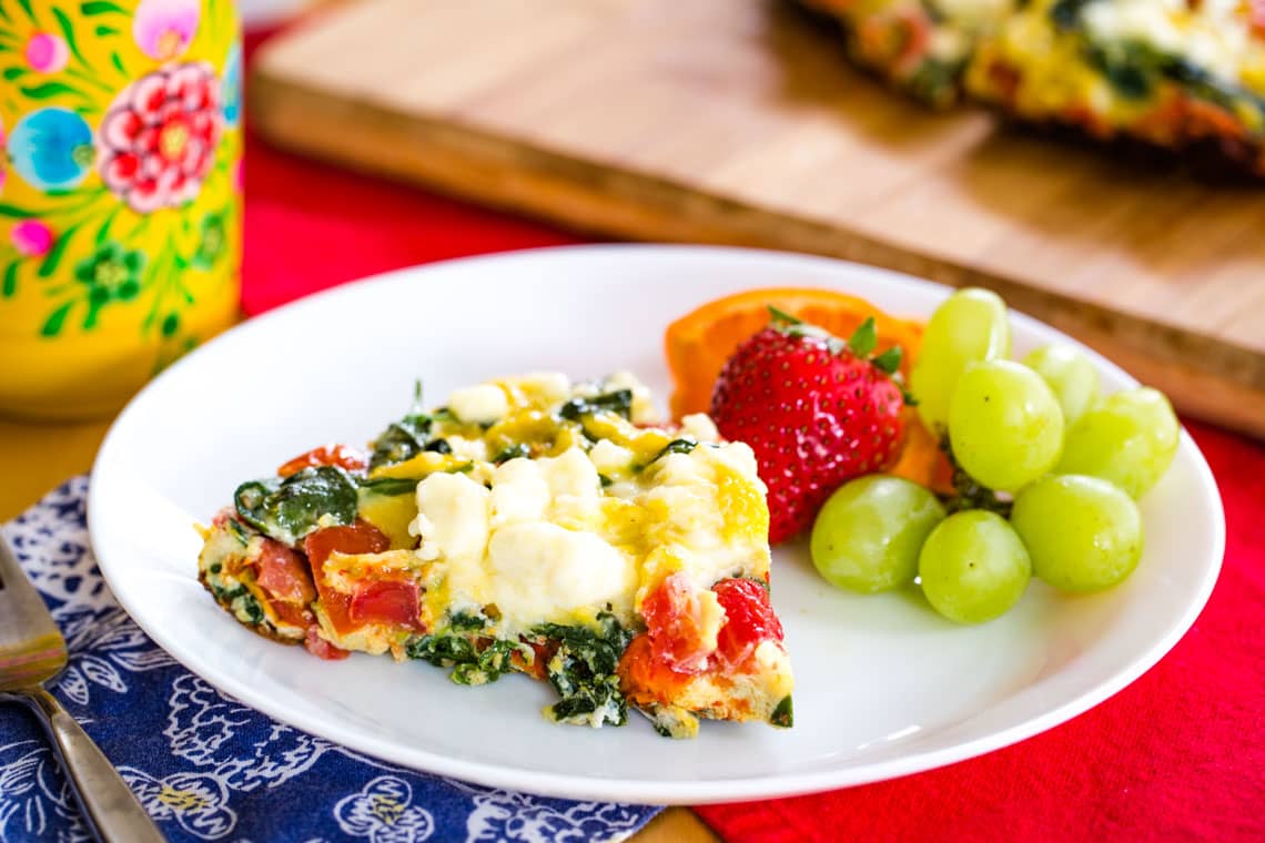 A slice of spinach frittata on a plate with fruit.