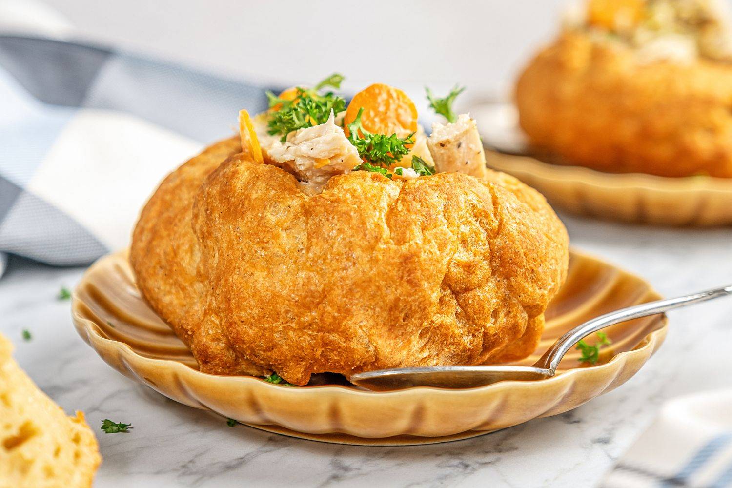 A bread bowl filled with chicken and vegetables on a light brown plate.