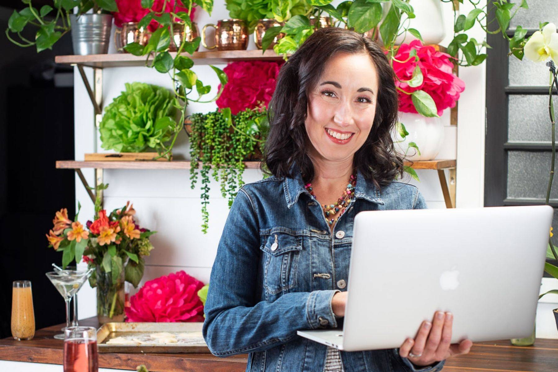 Smiling woman in a jean jacket holding a MacBook laptop.