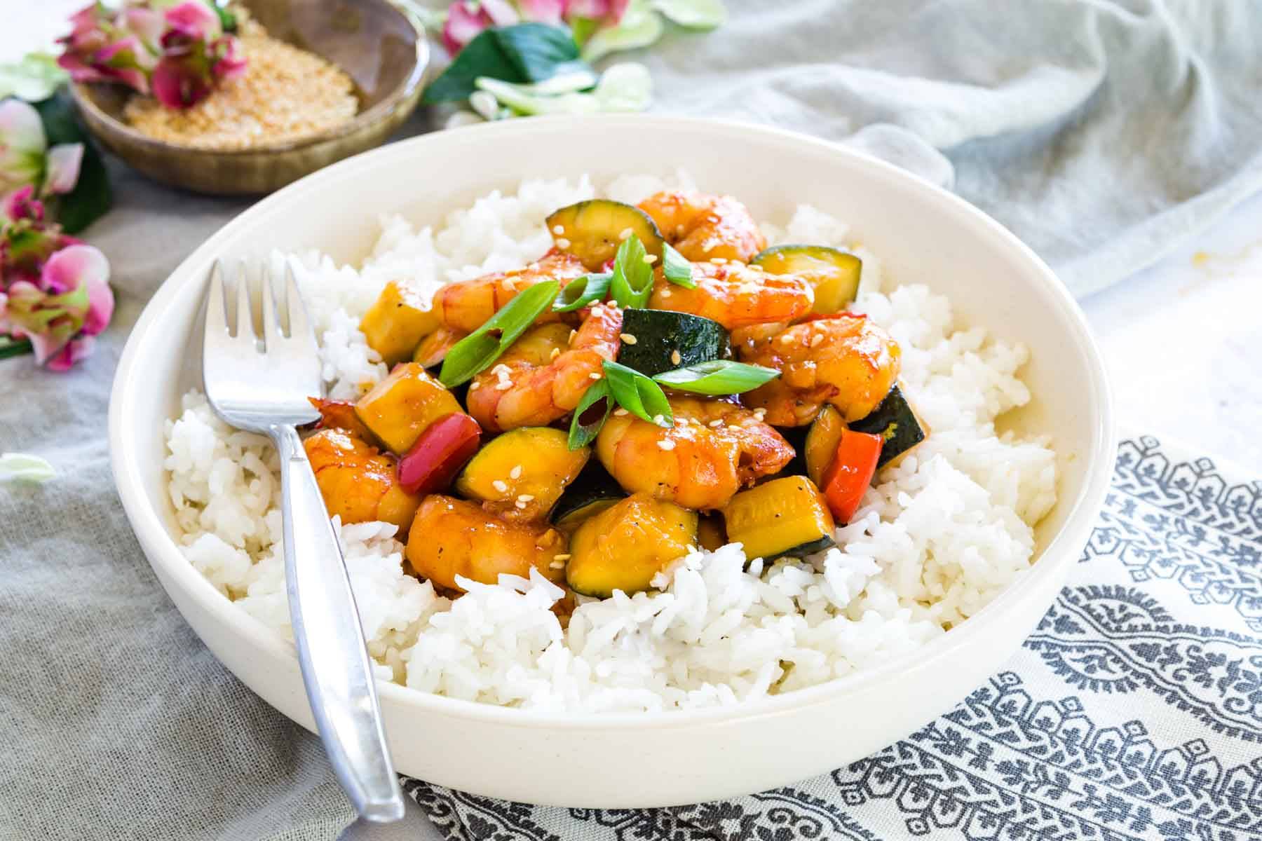 A dish of bourbon shrimp with zucchini and peppers served over white rice.