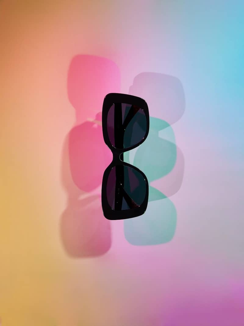 Black sunglasses casting colorful shadows on a gradient background.