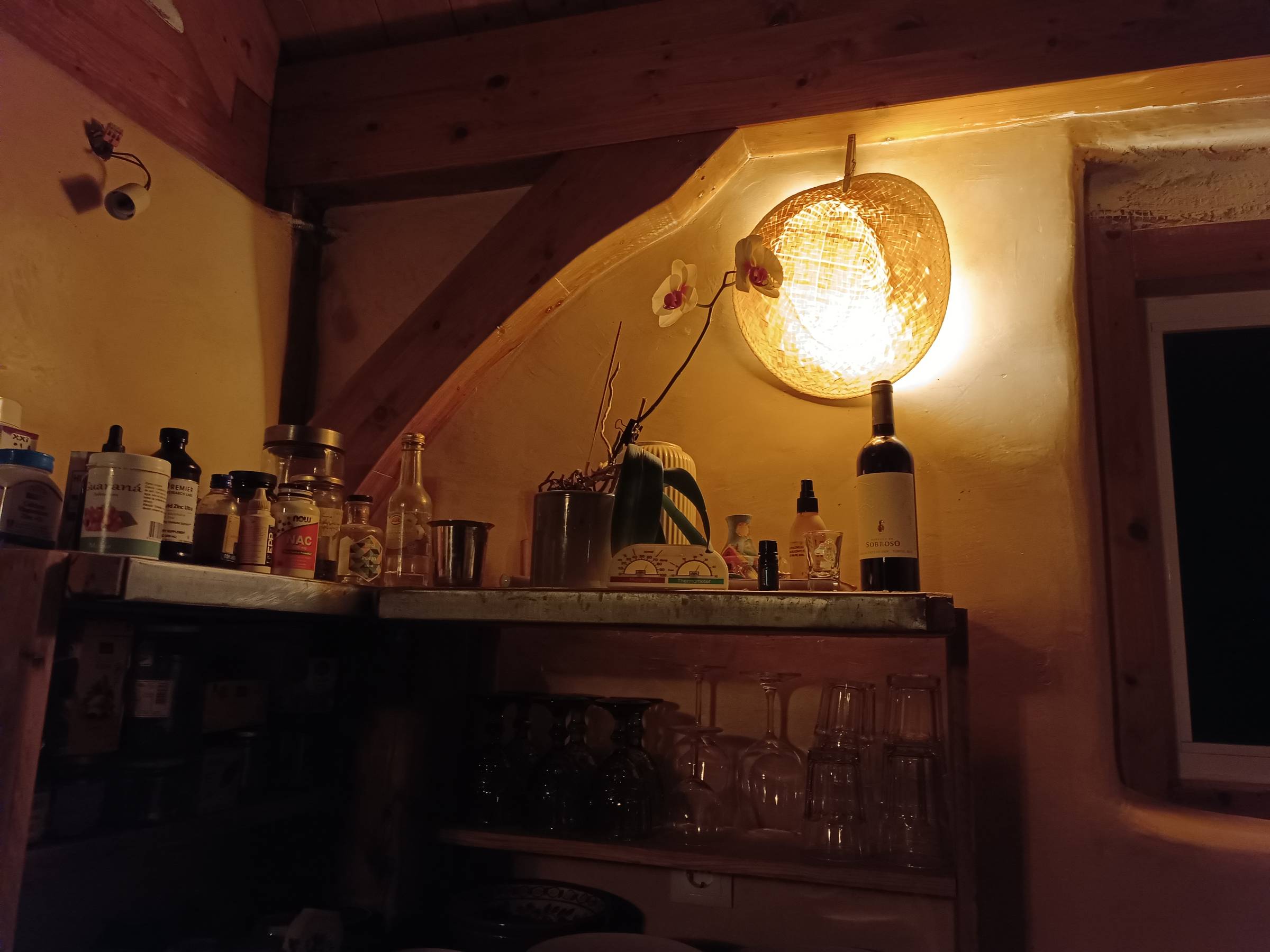 Warmly lit interior in Portugal with wooden beams, shelves, bottles, and a glowing woven pendant lamp.