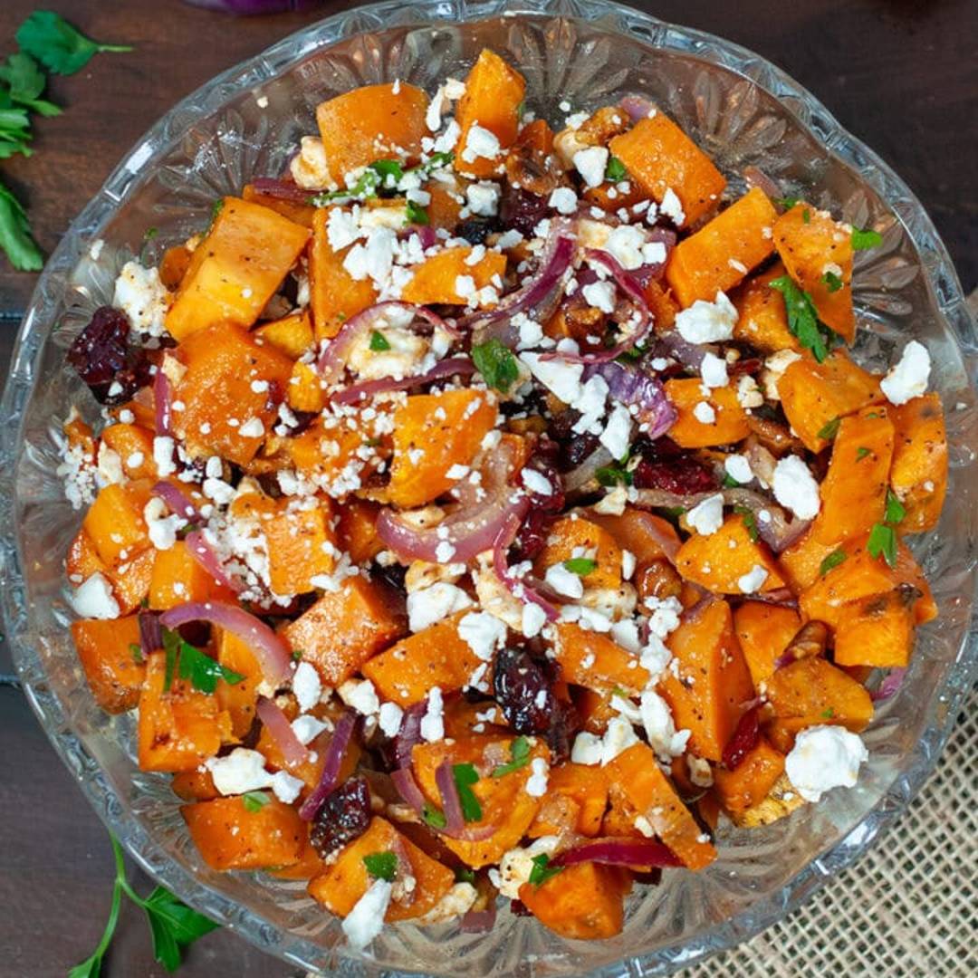 A bowl of sweet potato salad topped with feta cheese, green onions, and fresh parsley