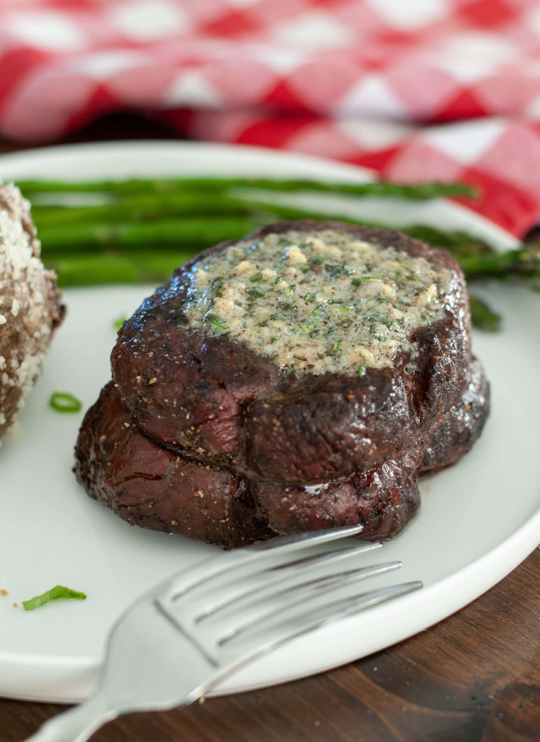 A filet perfectly grilled with compound butter full of herbs melting on top. 