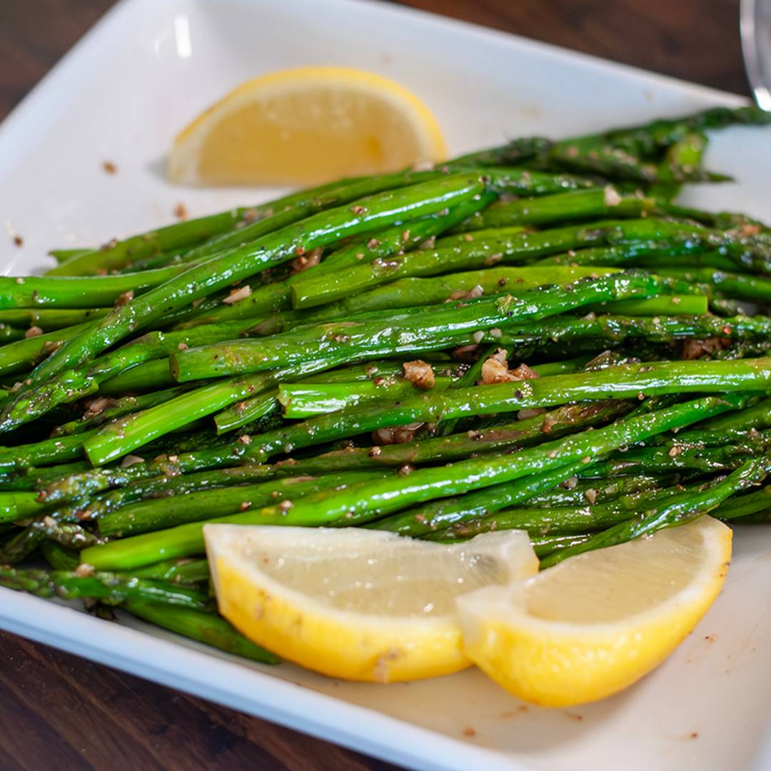A plate of sauteed Asparagus garnished with lemon and garlic. 