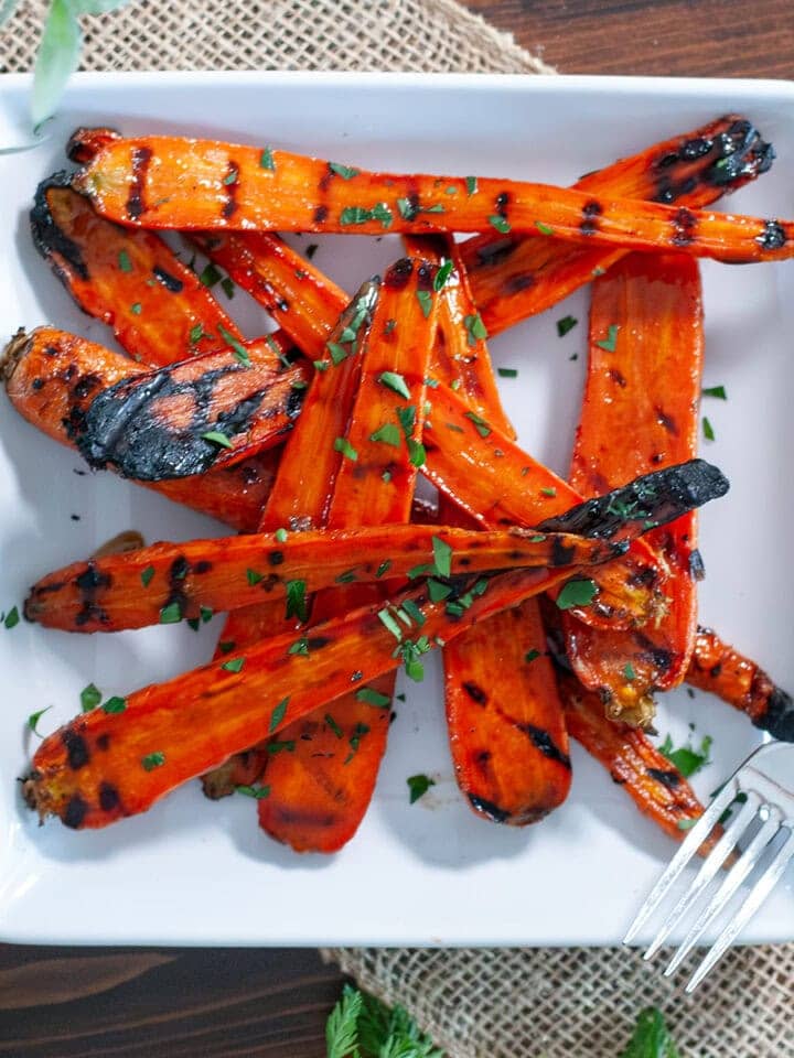 Beautiful, glazed carrots that have been grilled on a white serving platter. 