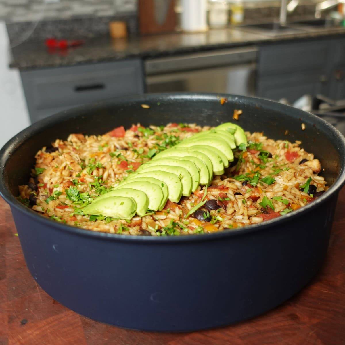 A pan of cajun chicken and rice with fresh avocado on top. 
