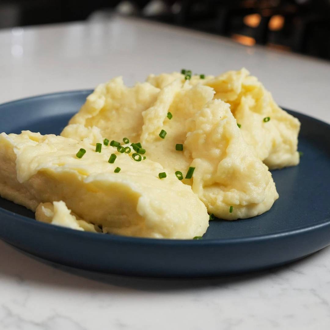 A large serving of creamy mashed potatoes garnished with fresh chives.
