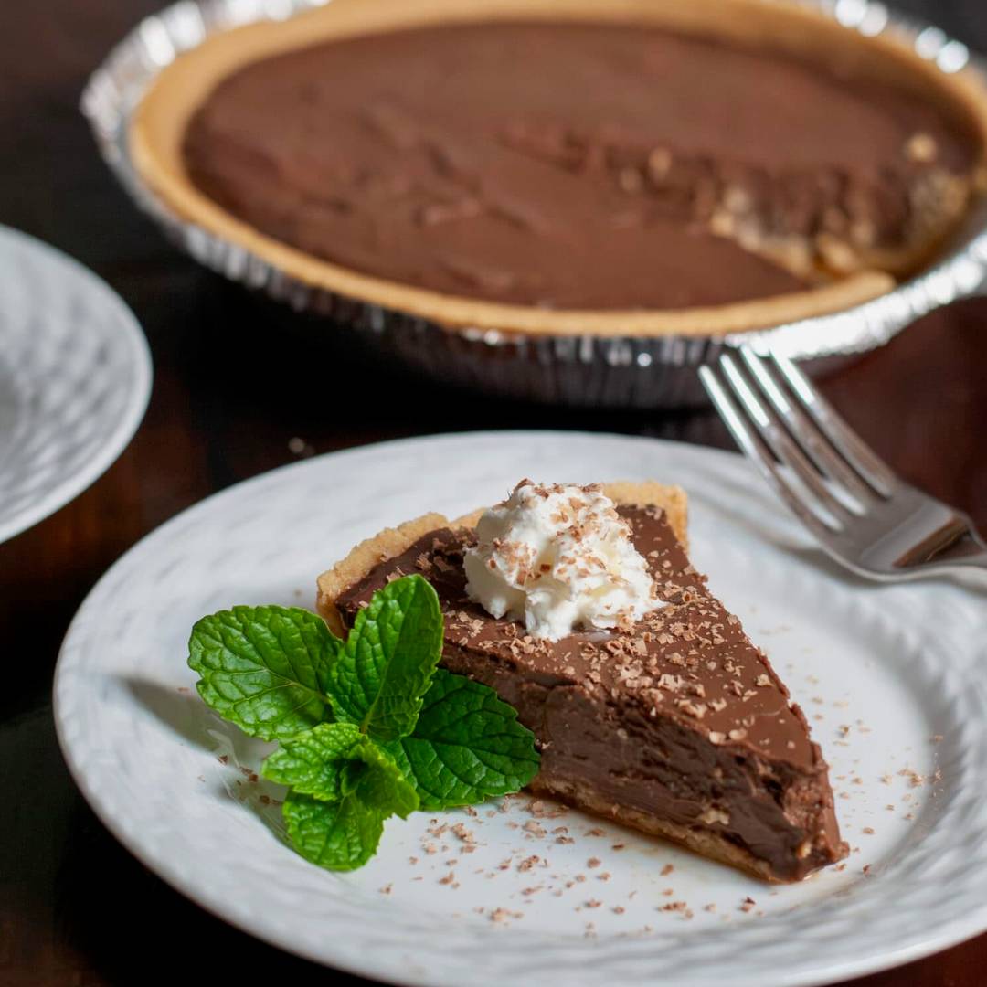 A slice of fresh chocolate pie topped with whipped cream and garnished with fresh mint. 