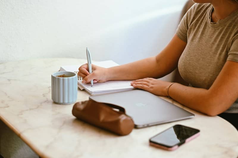 A person writing in a planner with a pen at a marble table