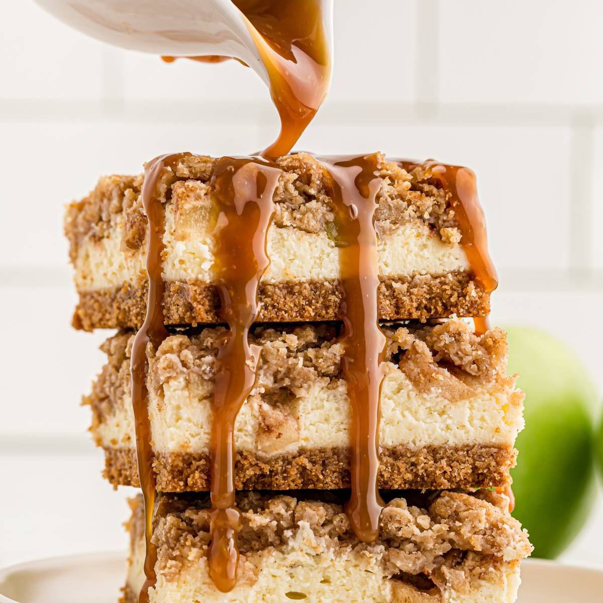 caramel sauce pouring over a stack of caramel apple cheesecake bars
