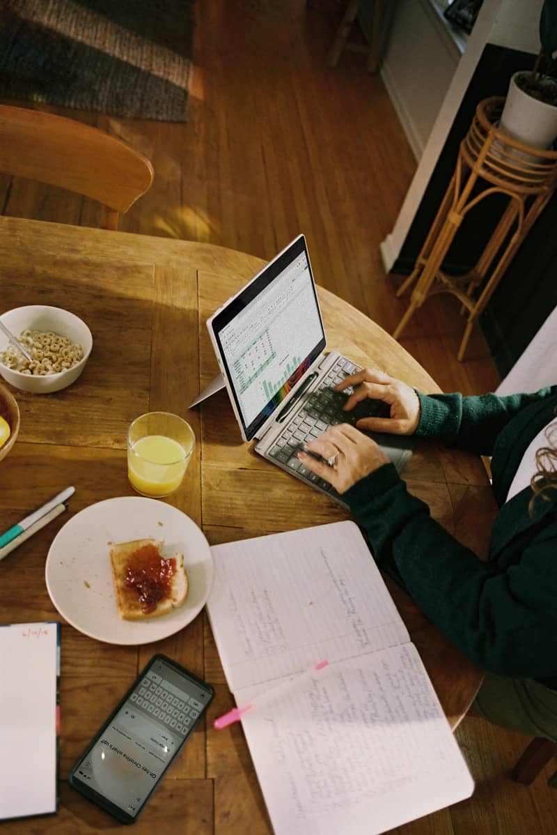 Person working on laptop at wooden table with breakfast