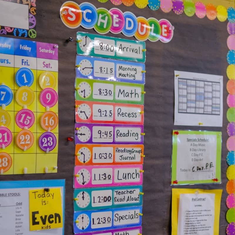 A colorful classroom schedule board with clock icons and daily activity labels