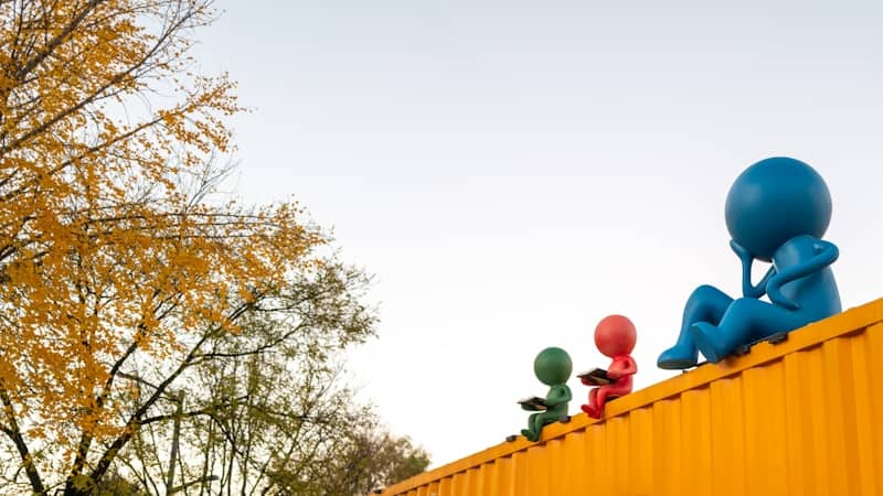 Three colorful figures sit on a yellow structure.