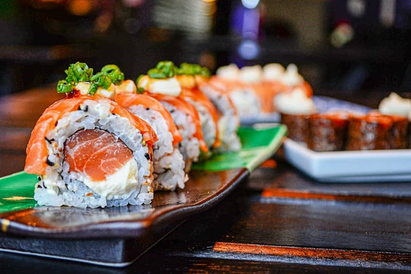 Salmon sushi rolls topped with cream cheese and green onions on a plate