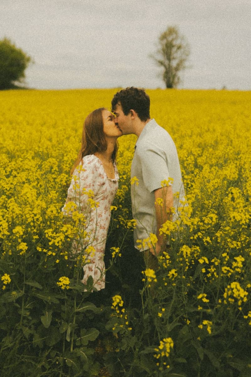 Couple sharing a kiss in a vibrant field of flowers.