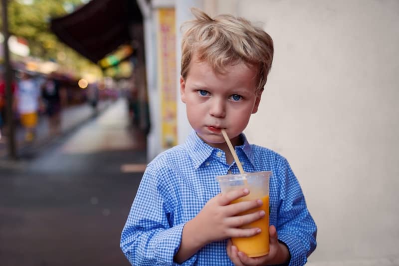 A young boy in a blue shirt drinks orange juice.