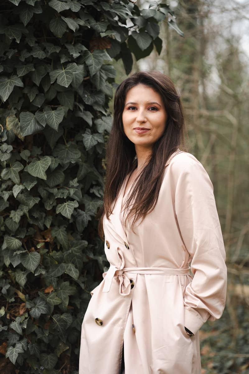 A woman poses outdoors in a trench coat.