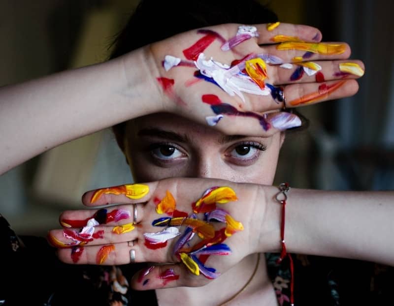 Artist with paint-covered hands peeking through fingers.
