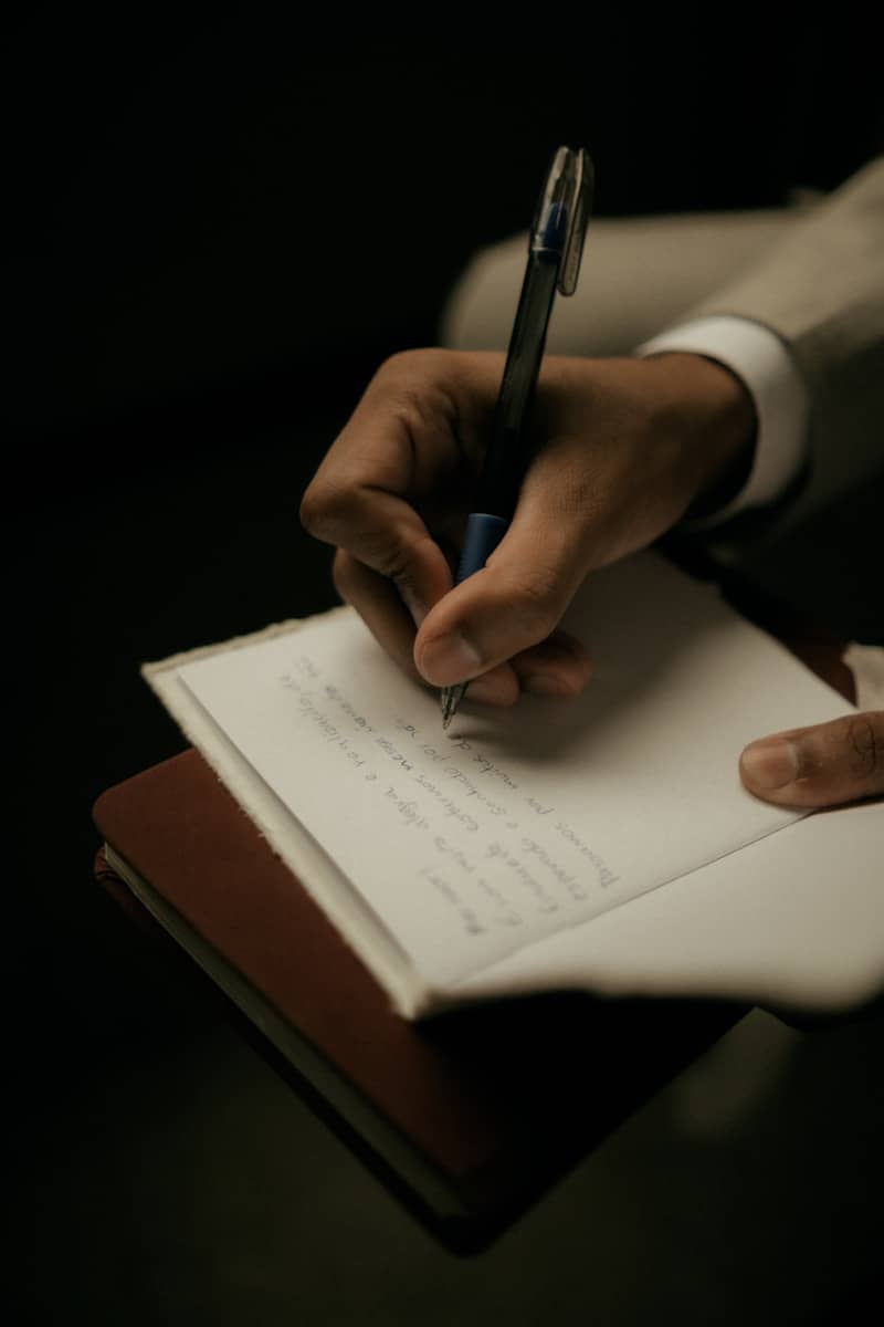 A person writing in a notebook with a pen.