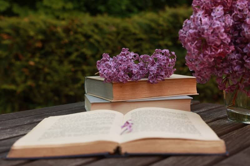 Stack of books with purple flowers and greenery.