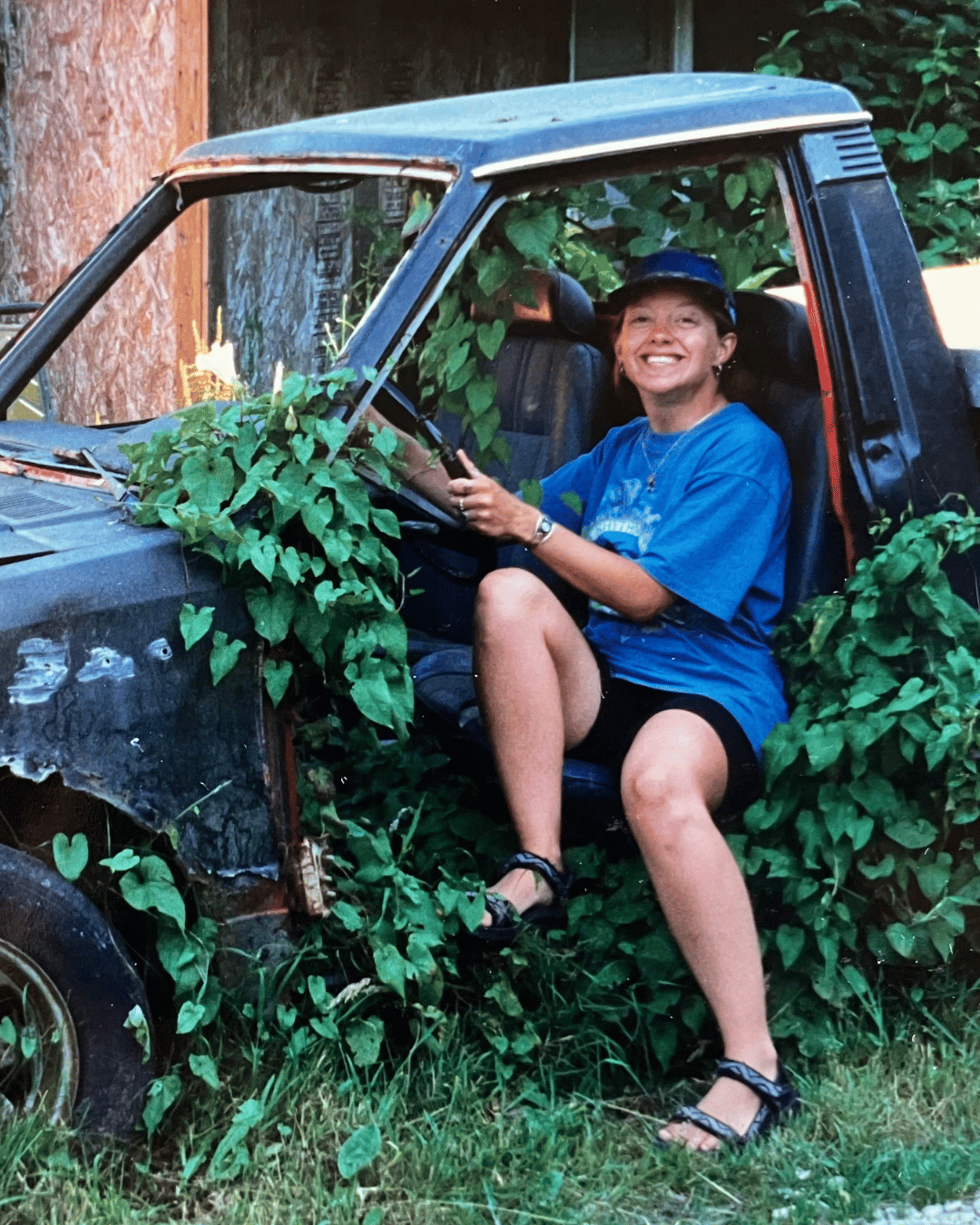 Me in my full moon circle days. (Young woman sitting in driver's seat of abandoned pickup truck covered in vines.)
