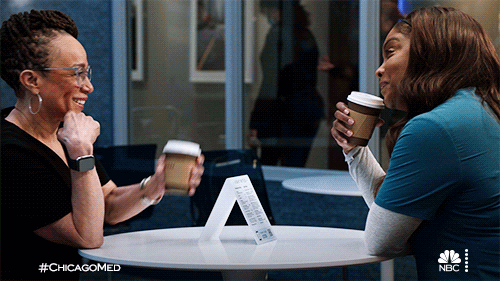 Two people sitting down and clinking their coffee cups together