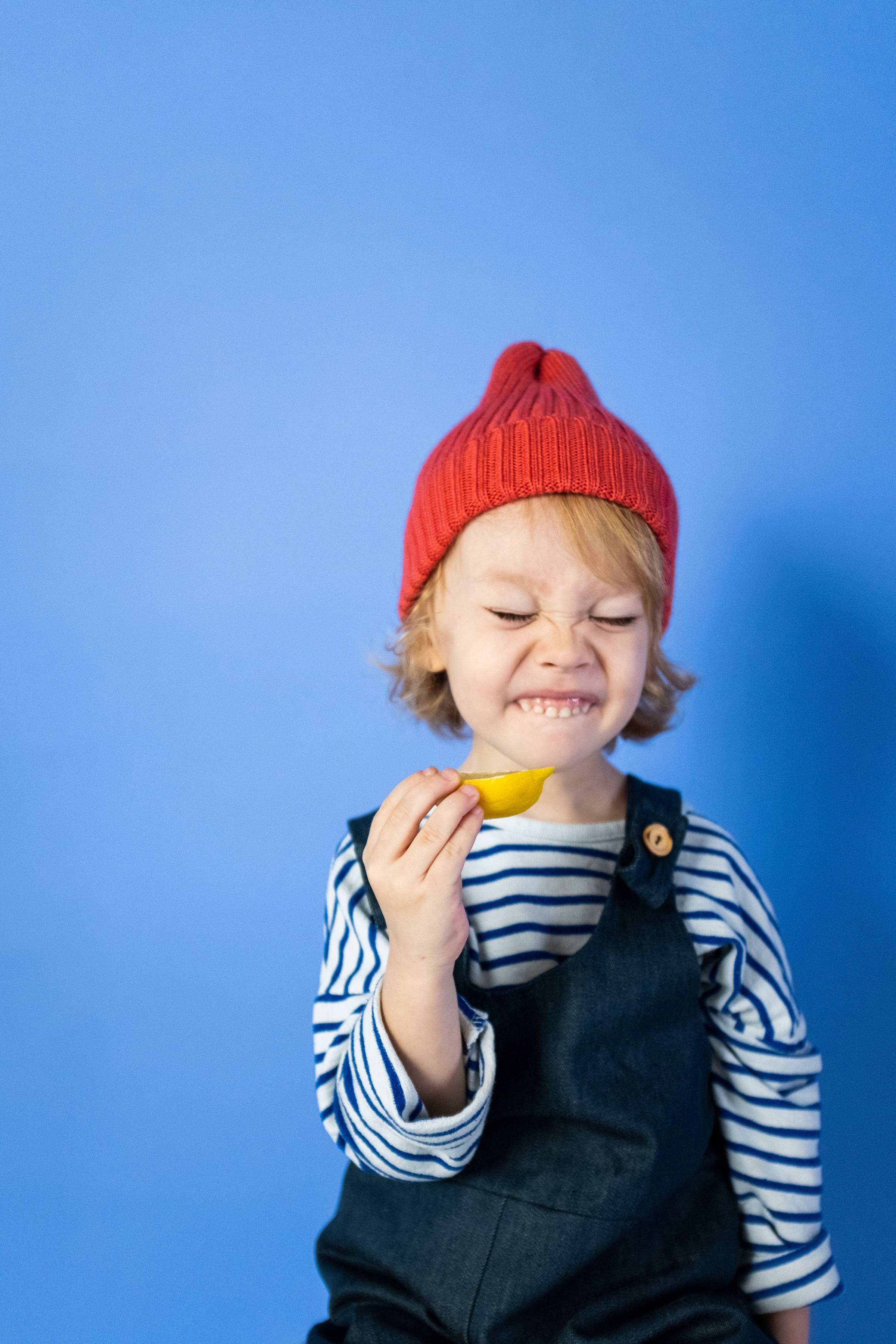 A young child making a funny, squinched-up face while taking a bite of a fresh lemon slice
