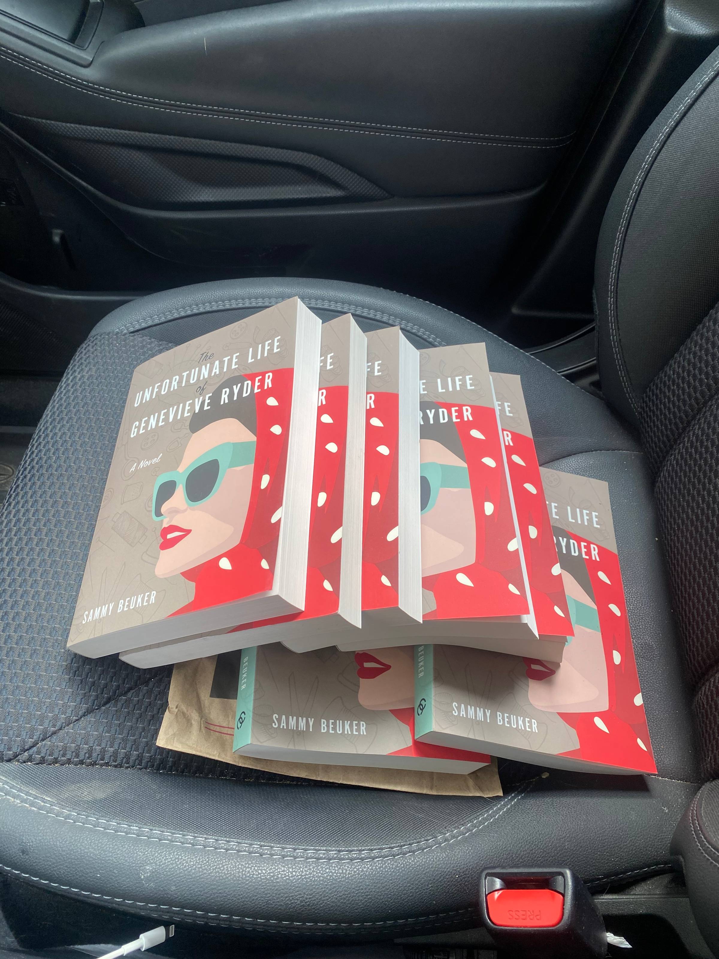 A stack of books sits on a car seat. 