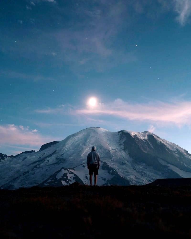 man standing on grass field overlooking mountain