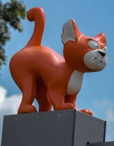 A fun orange cat statue stands on a rooftop.