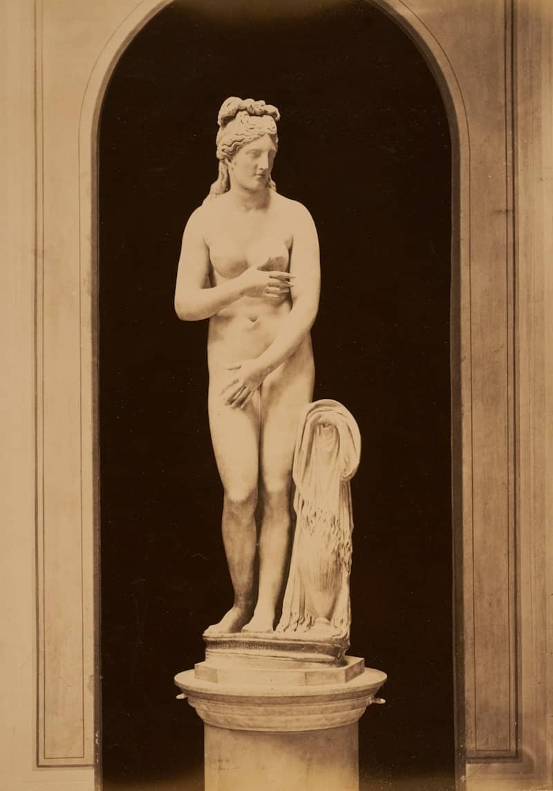 A nude statue stands within an architectural arch.