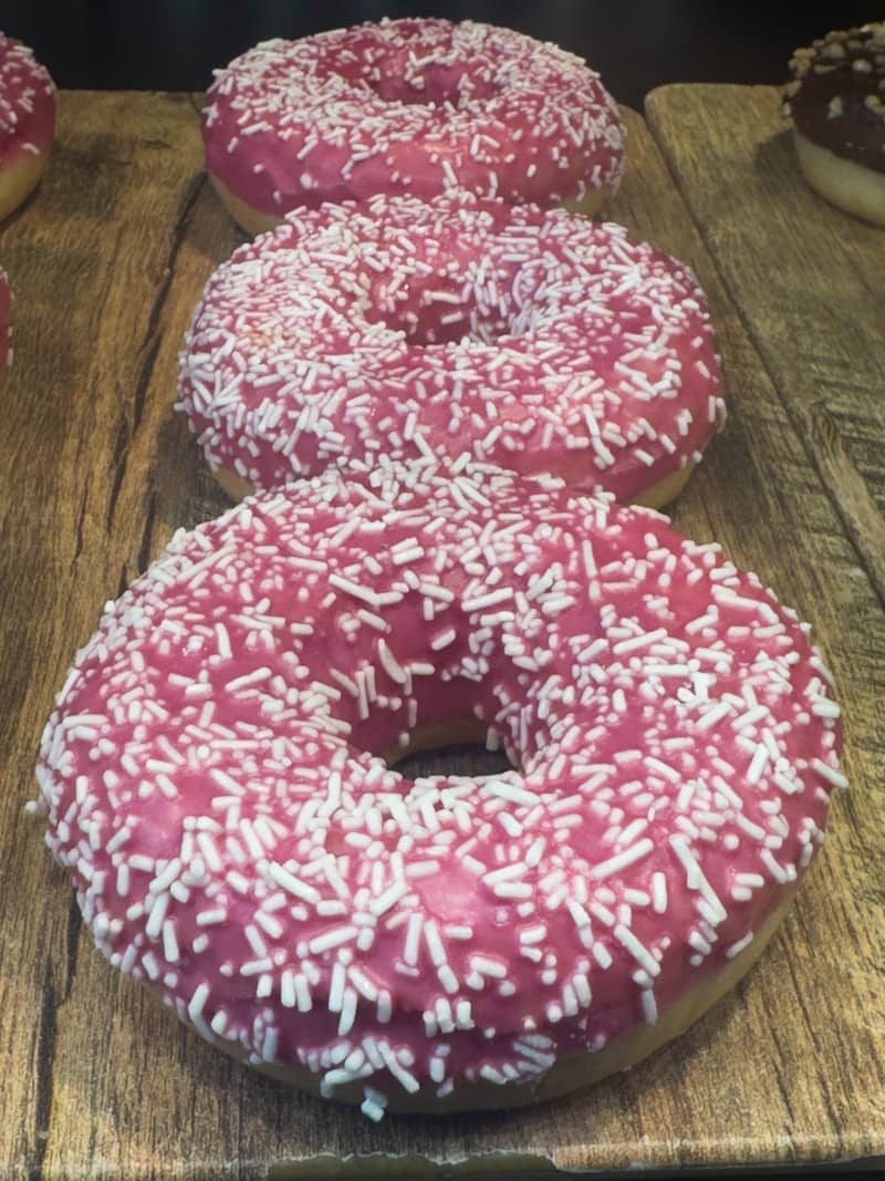 Three pink frosted donuts with white sprinkles