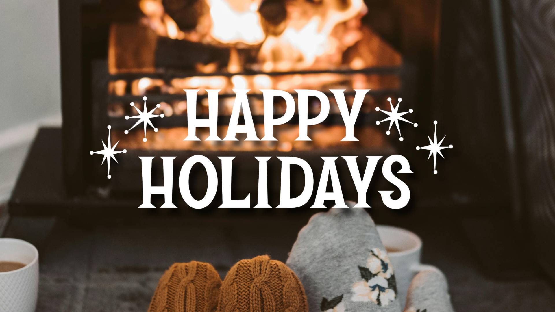 Happy Holidays text overlaid over slippered feet in front of a fire
