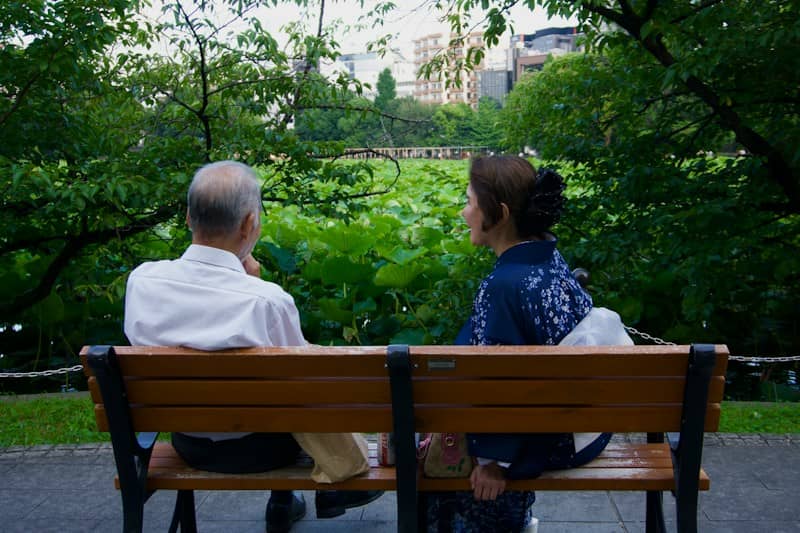 A man and a woman on a wooden bench facing a lotus pond