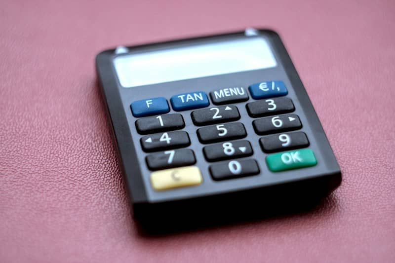 A black electronic banking card reader with a numeric keypad on a red surface