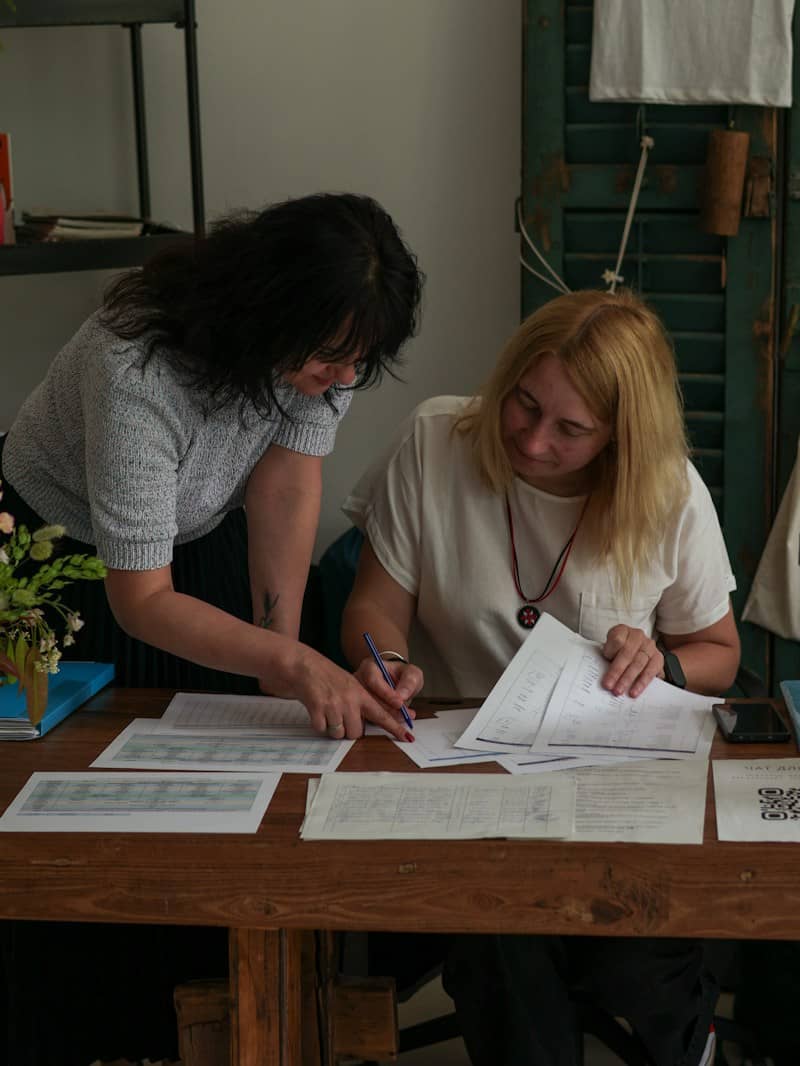 Two women reviewing documents together at a wooden table in a workspace